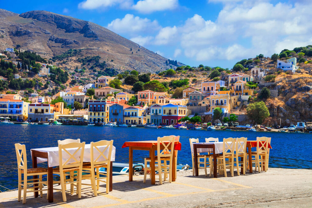 Charming Greek Seaside Village with Colorful Homes and Scenic Dining Wallpaper