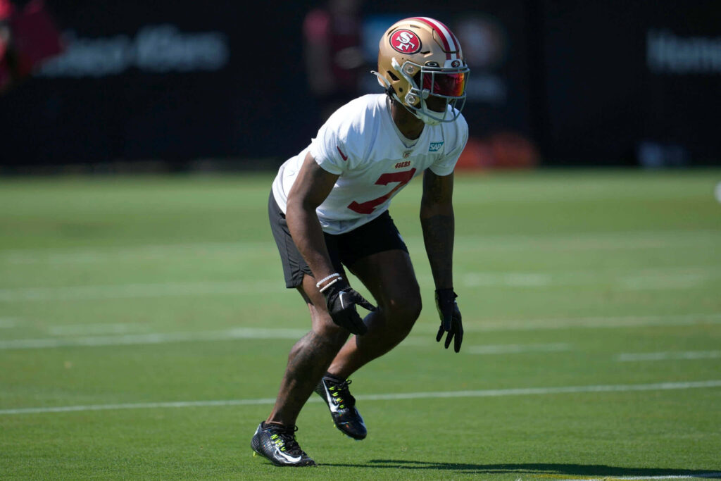 Charvarius Ward in San Francisco 49ers red gold helmet and white uniform during NFL training Wallpaper