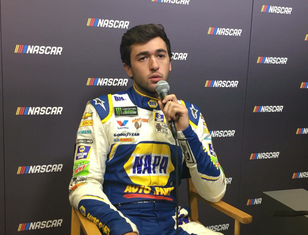 Chase Elliott in blue yellow NAPA racing suit at NASCAR press event with sponsor logos visible Wallpaper