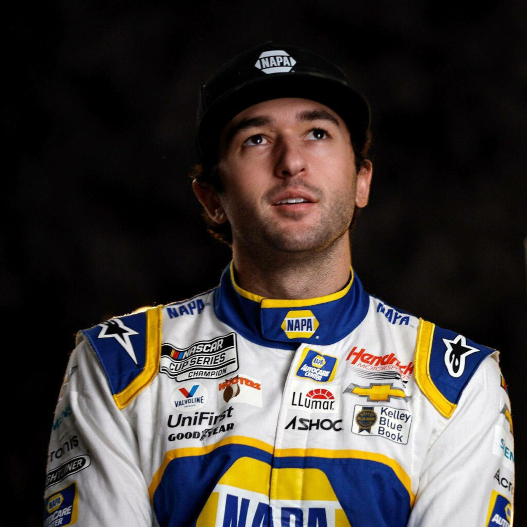 Chase Elliott in vibrant NAPA racing suit with focused expression on dark motorsport background Wallpaper