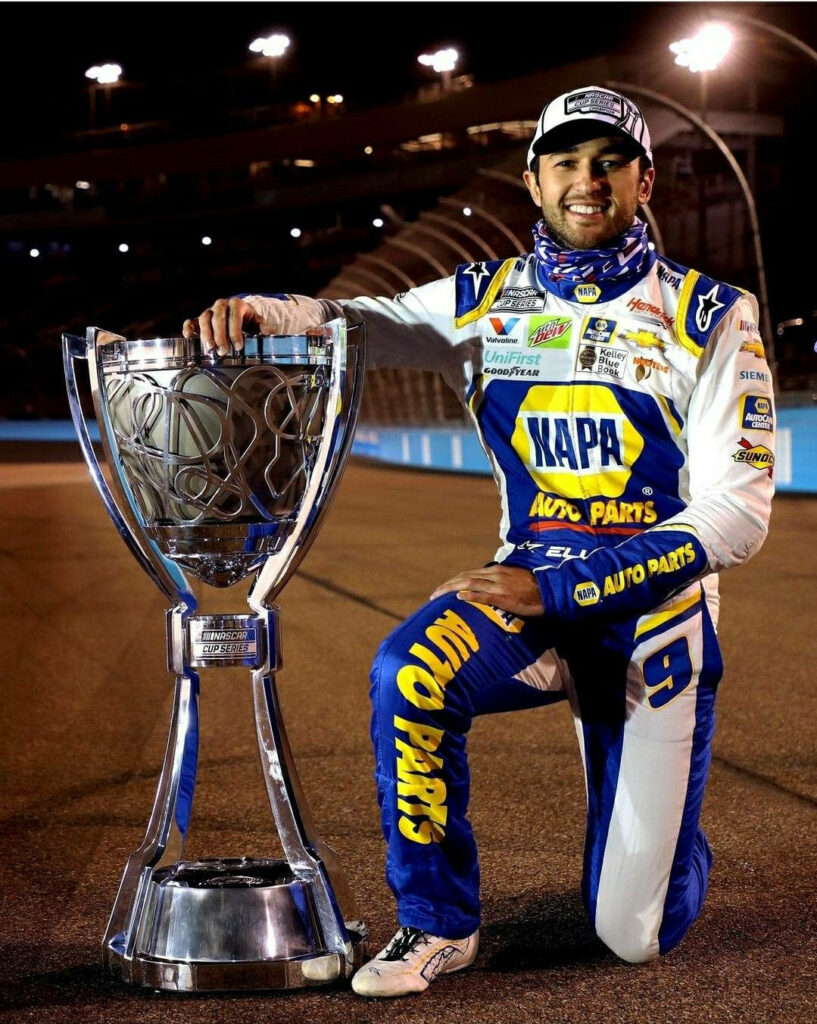 Chase Elliott in blue yellow NAPA racing suit with championship trophy on racetrack at night Wallpaper