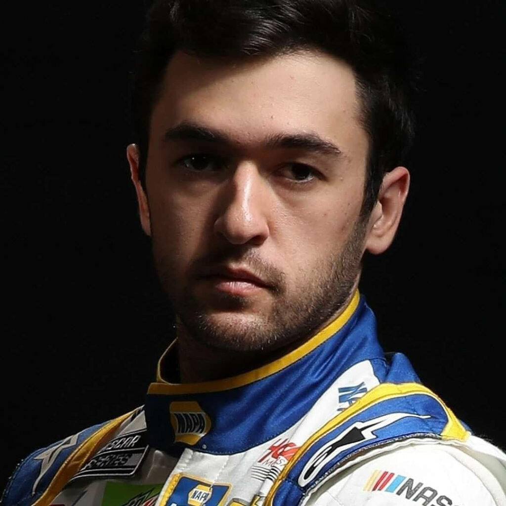 Close-up portrait of NASCAR driver Chase Elliott in racing suit with sponsor logos and dark background Wallpaper