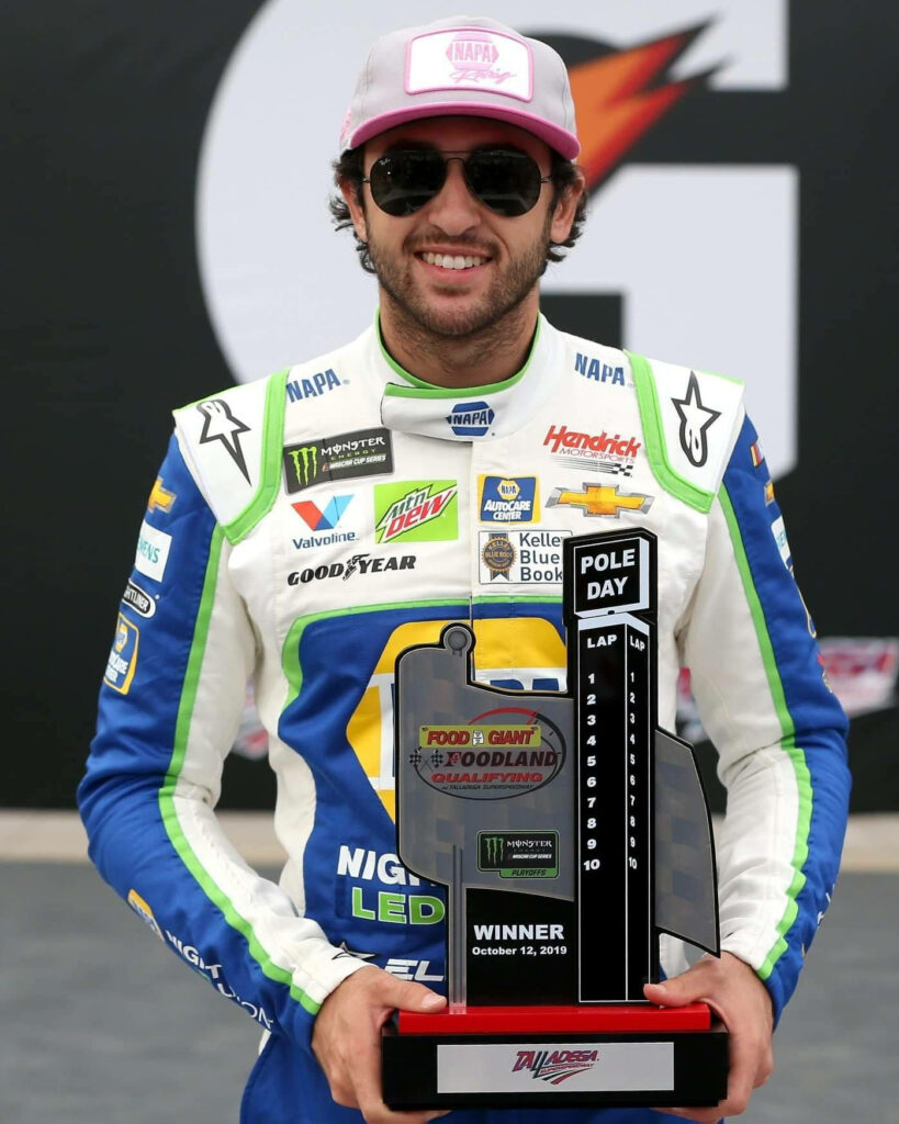 Chase Elliott in racing suit holding trophy at racetrack celebrating NASCAR victory wallpaper background