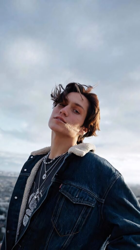 Chase Hudson in denim jacket with shearling collar against soft cloudy sky wallpaper background