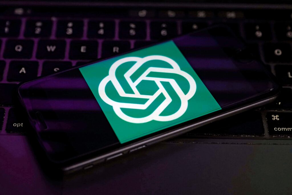 ChatGPT wallpaper on smartphone with green white OpenAI logo over purple backlit laptop keyboard