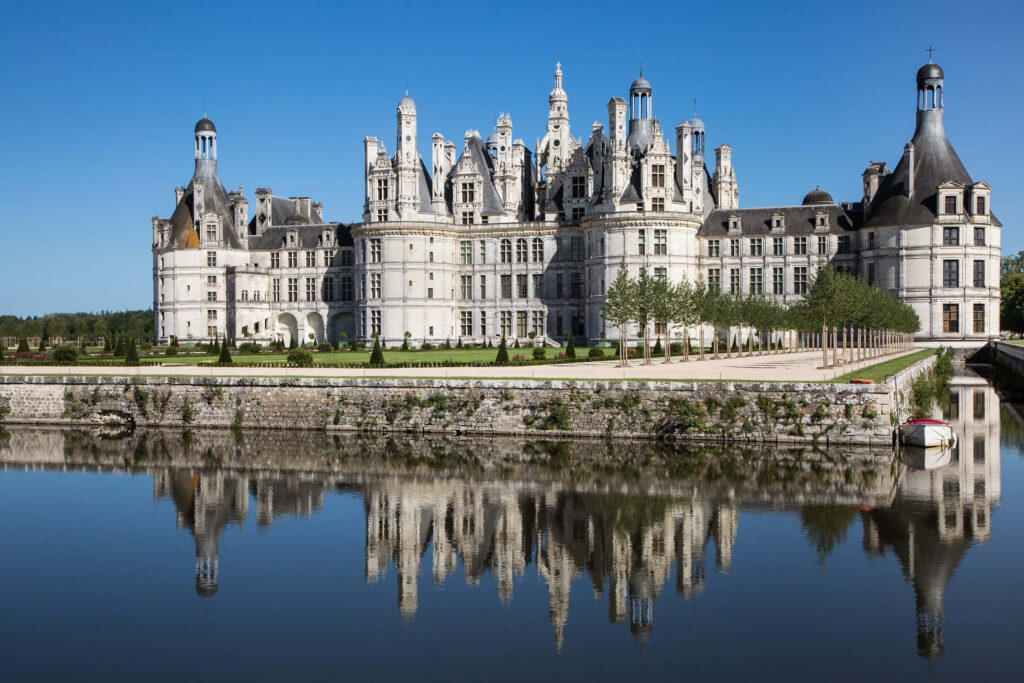 Château de Chambord reflected in calm river under clear sky with Renaissance architecture and gardens Wallpaper