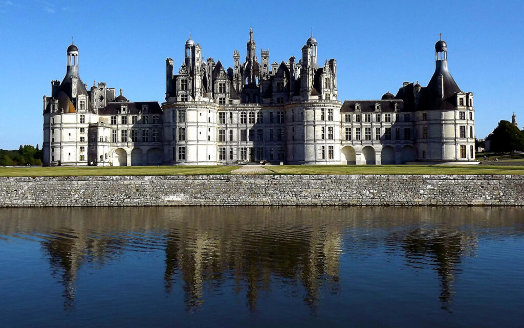 Château de Chambord Renaissance castle with intricate towers reflected in calm water under blue sky Wallpaper