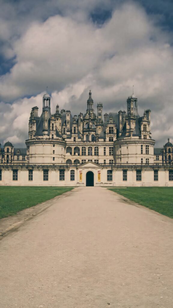 Château de Chambord Renaissance castle with ornate towers under dramatic cloudy sky and green lawn Wallpaper