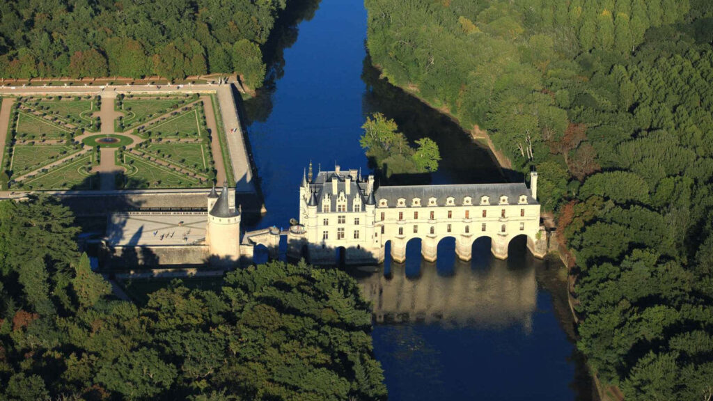 Aerial view of Château de Chenonceau with Renaissance arches over river surrounded by lush gardens Wallpaper