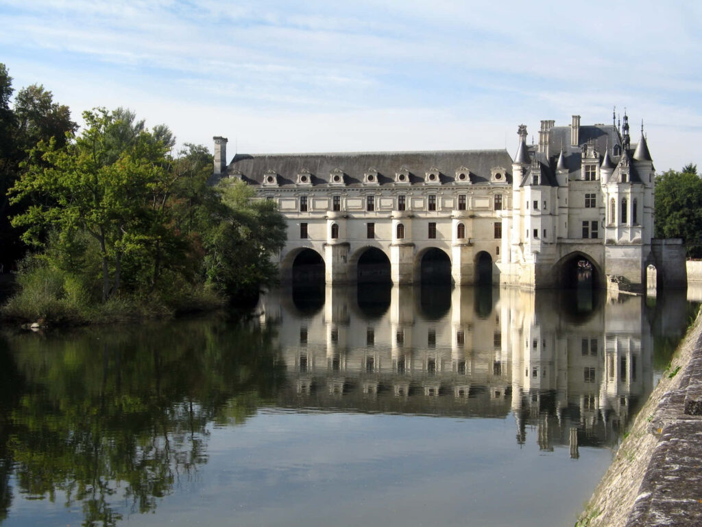 Château de Chenonceau castle over calm river with lush greenery reflecting historic architecture Wallpaper
