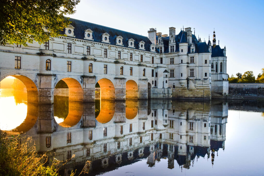 Château de Chenonceau in golden sunlight reflected in calm river with Renaissance architecture Wallpaper