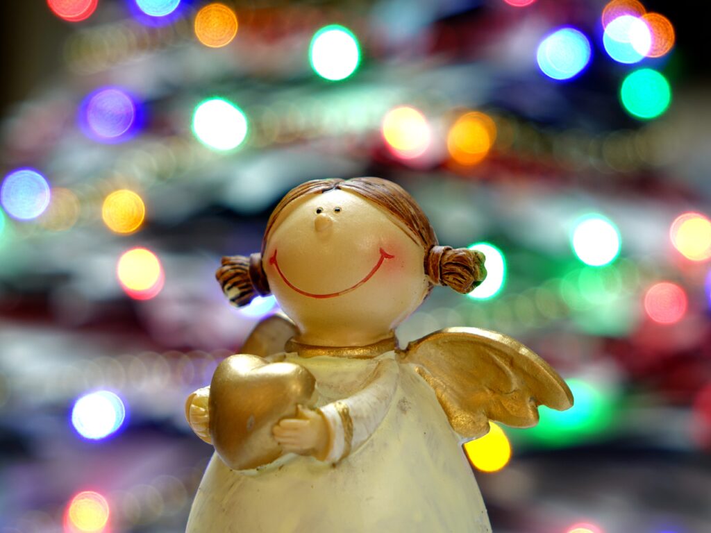 Cheerful Angel Statue with Heart Against Colorful Christmas Lights Wallpaper