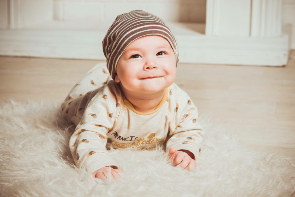 Charming baby with cheeky smile in cozy striped hat and playful pajamas on soft rug wallpaper