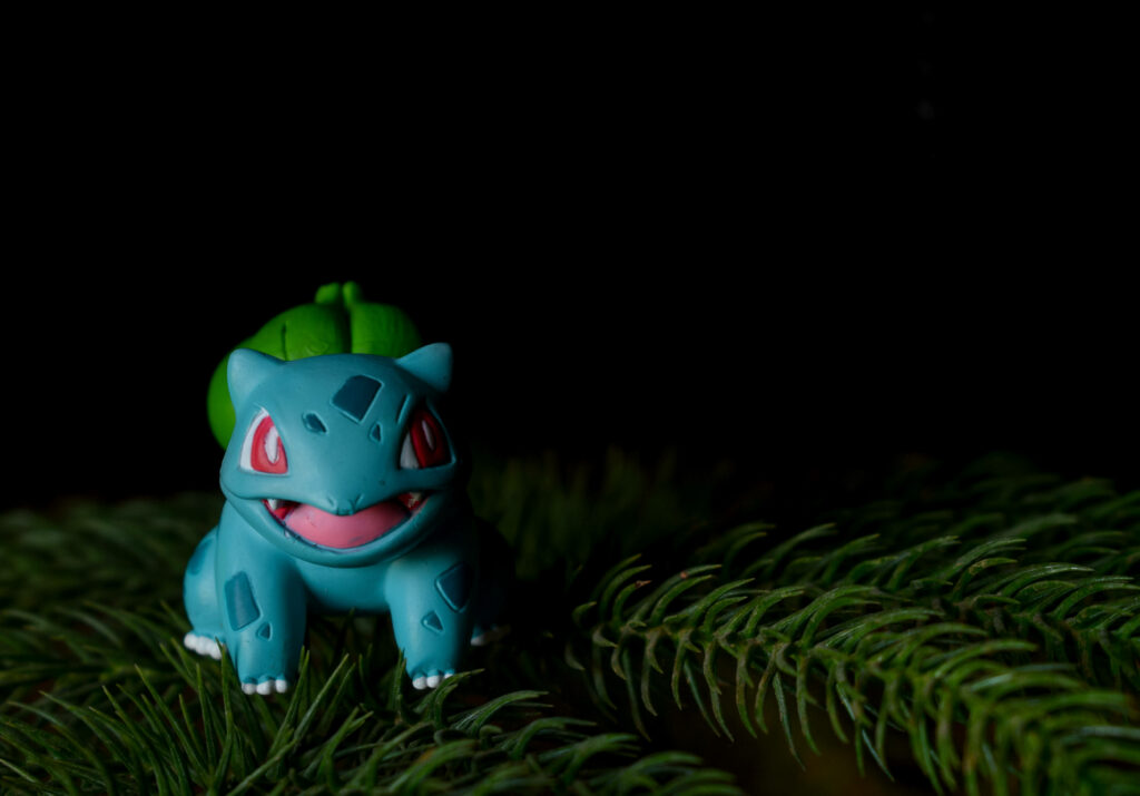 Cute Bulbasaur toy among pine needles with vibrant colors creating a cozy forest vibe Wallpaper