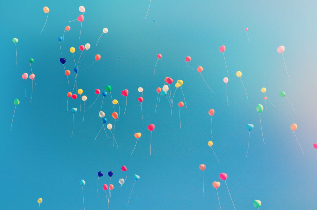 Colorful balloons floating against a soft blue sky gradient cheerful uplifting wallpaper background