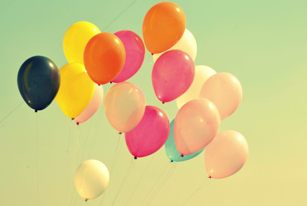 Colorful party balloons floating against a pastel sky cheerful festive wallpaper background