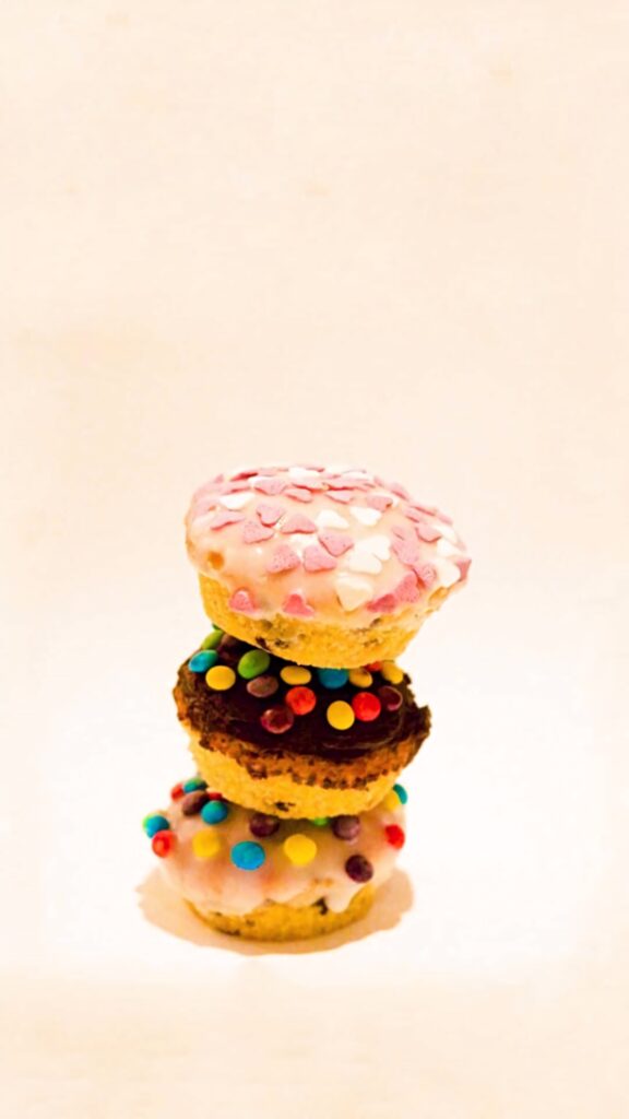 Stack of colorful sprinkled cupcakes with heart toppings on creamy pastel background wallpaper
