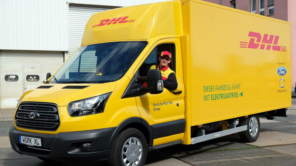 Cheerful DHL driver in yellow electric van outside modern building eco-friendly urban delivery Wallpaper