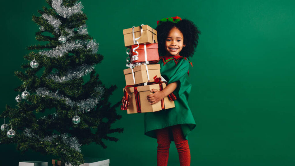 Cheerful Elf Child with Christmas Presents by Tree - Festive Scene Wallpaper