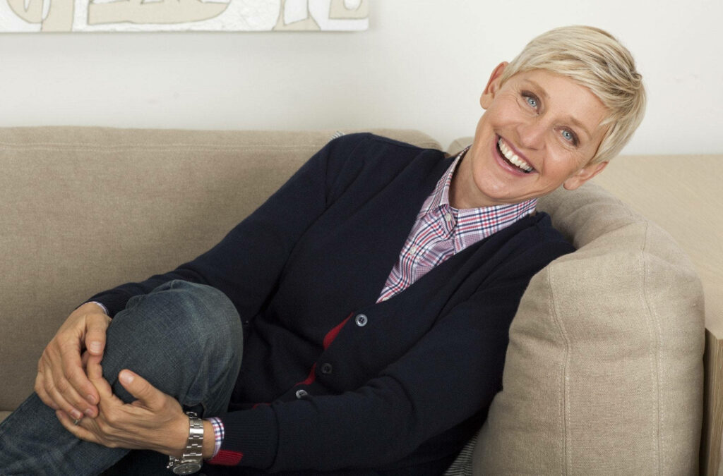 Ellen DeGeneres smiling warmly seated on beige couch casual relaxed setting wallpaper background