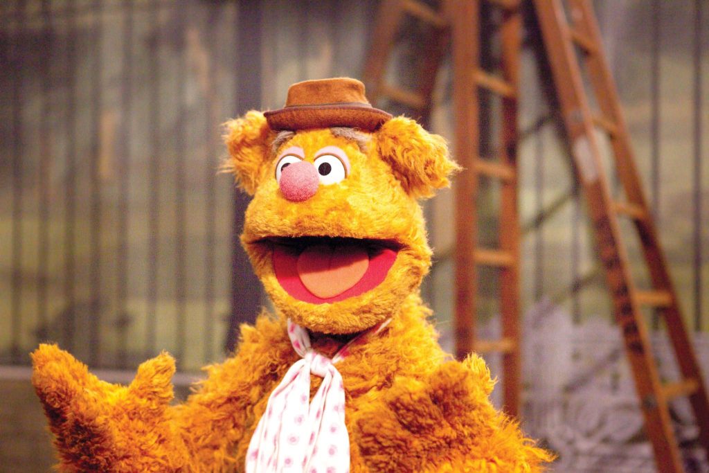 Cheerful Fozzie Bear wallpaper with brown hat white polka dot scarf rustic studio ladder background