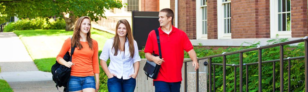 Three smiling students walk on sunny George Washington University campus with brick buildings Wallpaper
