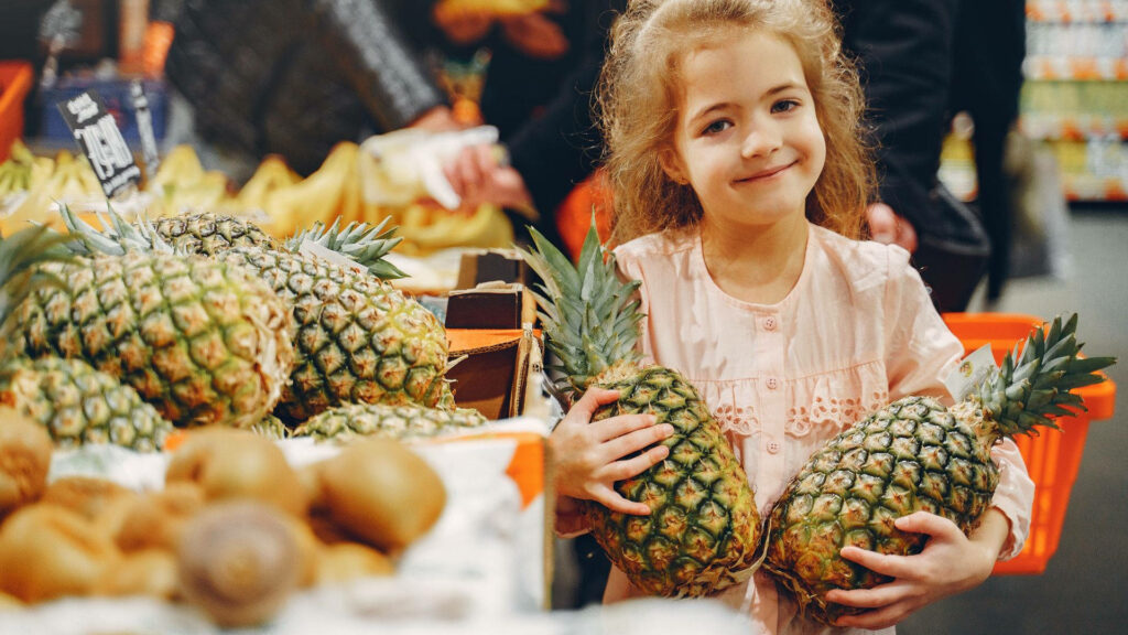Cheerful Girl with Fresh Pineapples in Vibrant Grocery Wallpaper