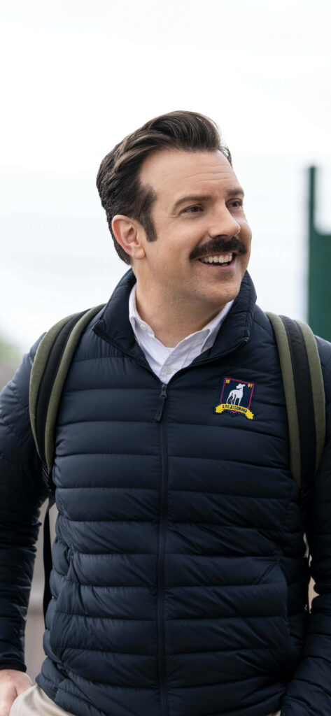Cheerful Man in Navy Jacket & Green Backpack: Ted Lasso Wallpaper
