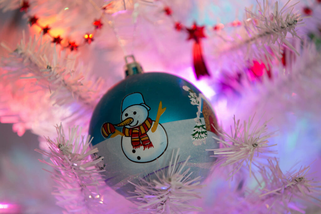 Colorful Snowman Ornament on Festive Christmas Tree Wallpaper