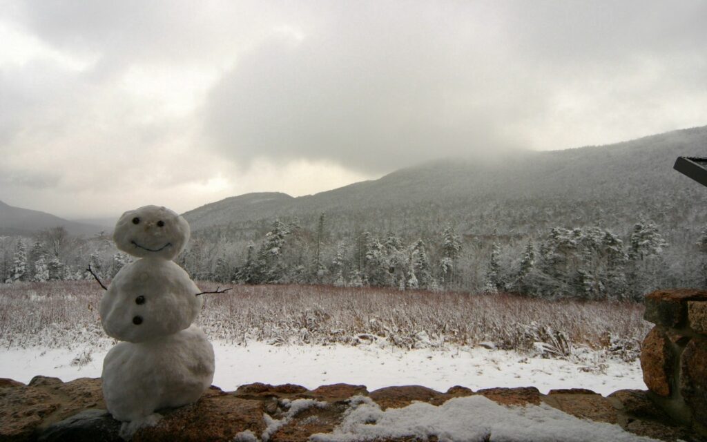 Cheerful snowman in snowy forest with foggy mountains stone wall frosty winter landscape wallpaper