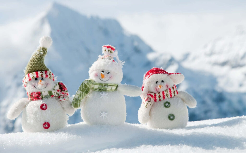 Cheerful Snowmen in Cozy Hats Amidst Snowy Mountain Landscape Wallpaper