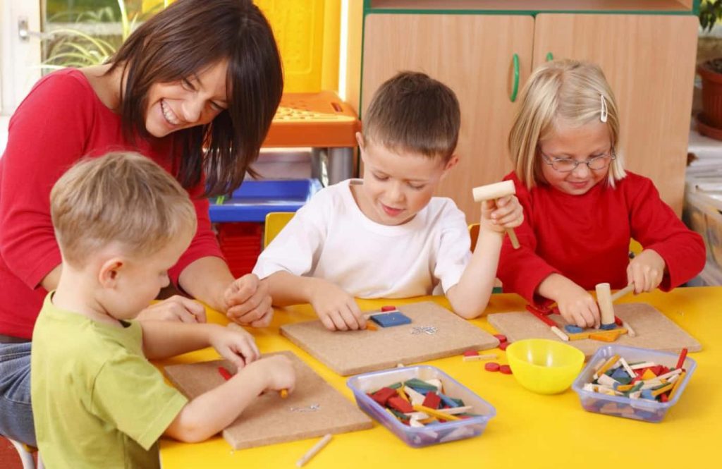 Teacher guiding children with colorful shapes on cork boards at yellow table learning wallpaper