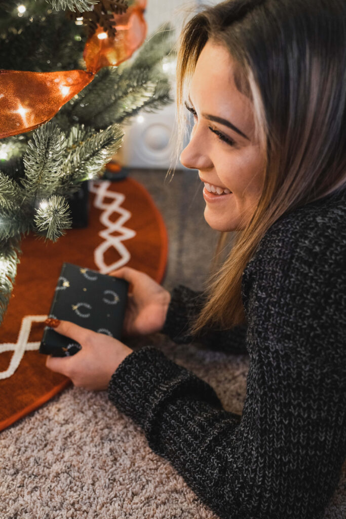 Cheerful Woman with Gift by Festive Christmas Tree Background Wallpaper