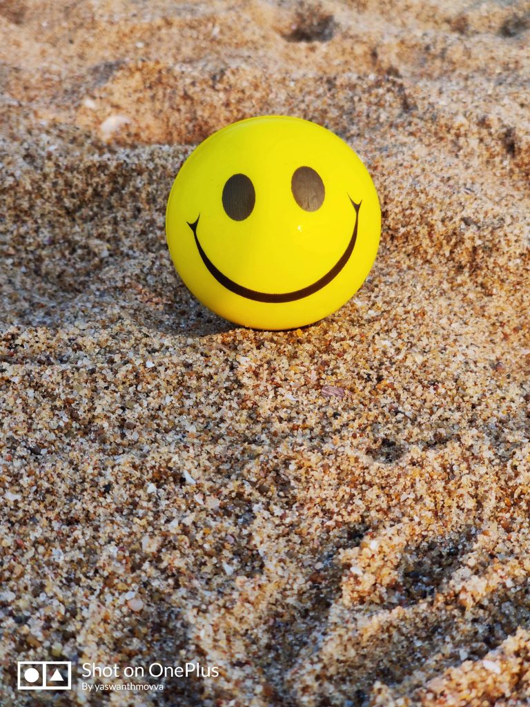 Smiley face ball on textured beach sand in sunlight vibrant yellow cheerful wallpaper background