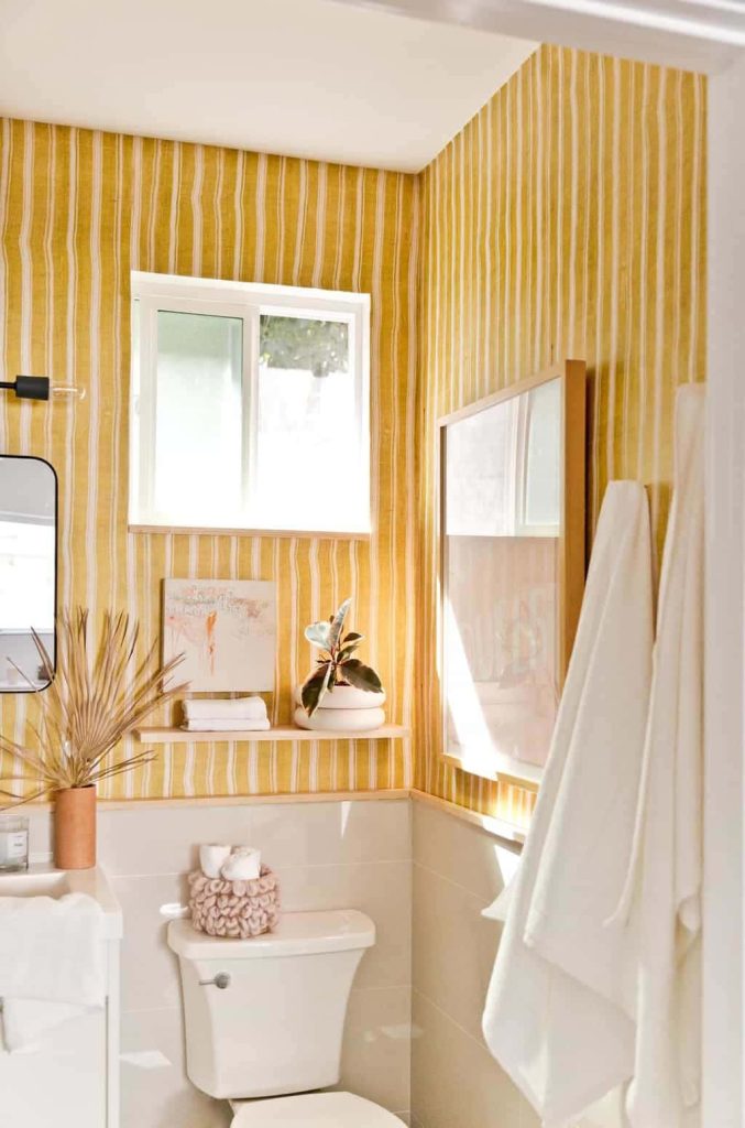 Cheerful bathroom with yellow white vertical striped wallpaper natural light and cozy accents