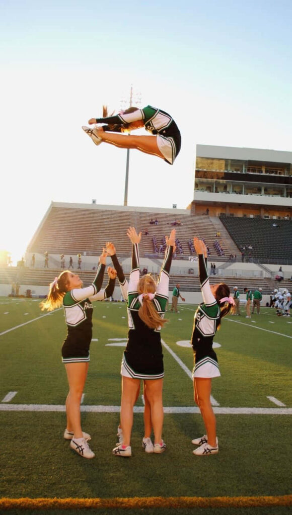 Dynamic Cheerleaders in Green & Black Synchronized Stunt at Sunset Wallpaper