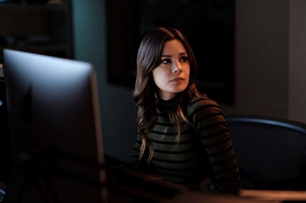 Chelsea Hobbs focused working at computer in dimly lit modern workspace with warm lighting background Wallpaper