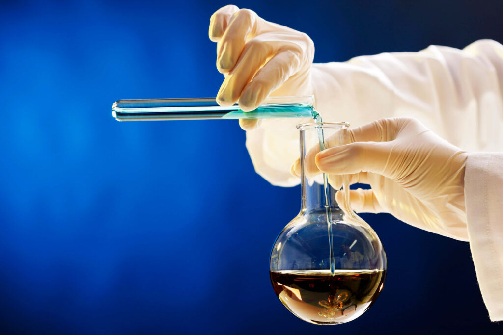 Gloved hands pouring vibrant blue liquid into flask in chemistry lab with blue gradient background Wallpaper