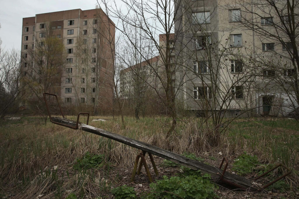Desolate Chernobyl playground with rusted seesaw overgrown grass abandoned apartments wallpaper
