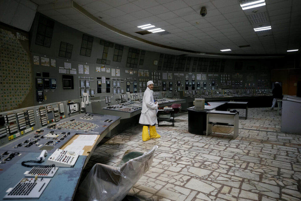 Worker in protective suit in dim Chernobyl control room with control panels and eerie atmosphere Wallpaper