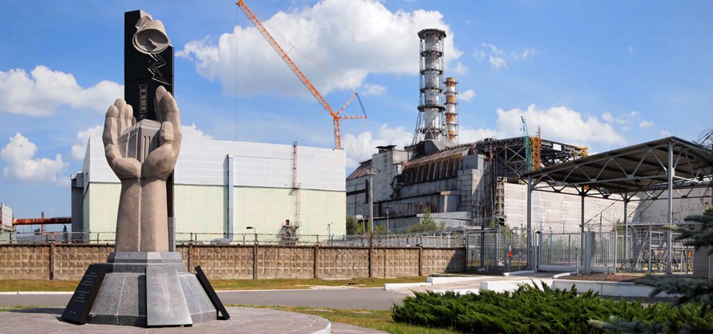 Chernobyl statue hands holding symbol with nuclear power plant and sarcophagus under blue sky Wallpaper