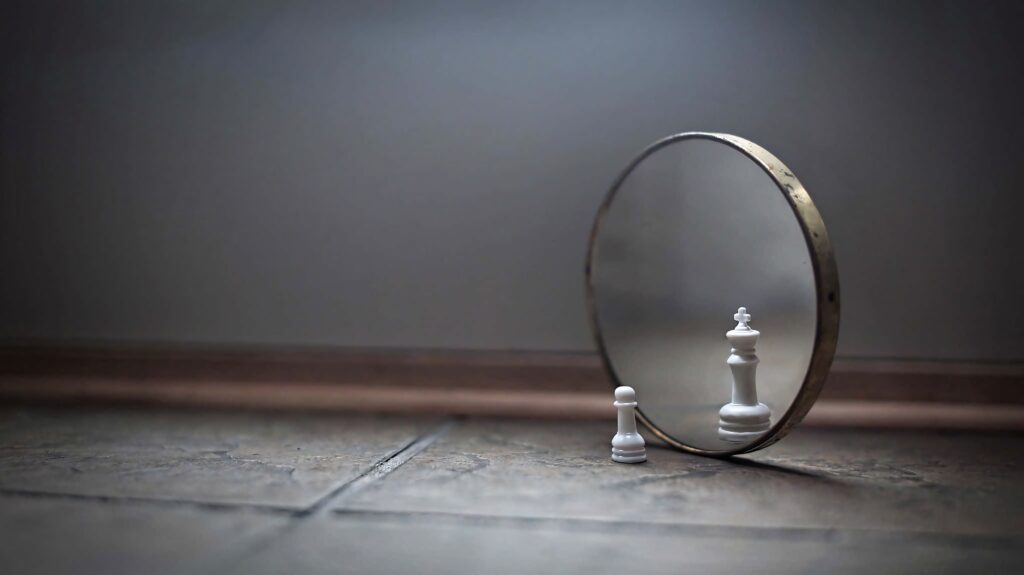 Chess pawn reflecting as powerful white queen in round mirror on tiled floor symbolizing ambition Wallpaper