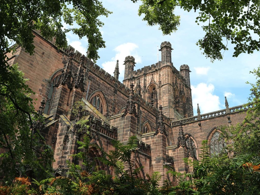 Chester Cathedral Gothic architecture with red sandstone under bright blue sky framed by greenery Wallpaper