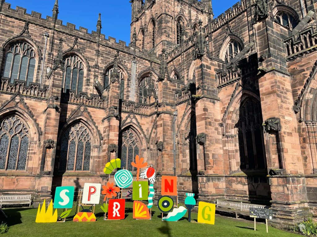 Chester Cathedral red sandstone gothic architecture with colorful spring sign on green lawn Wallpaper