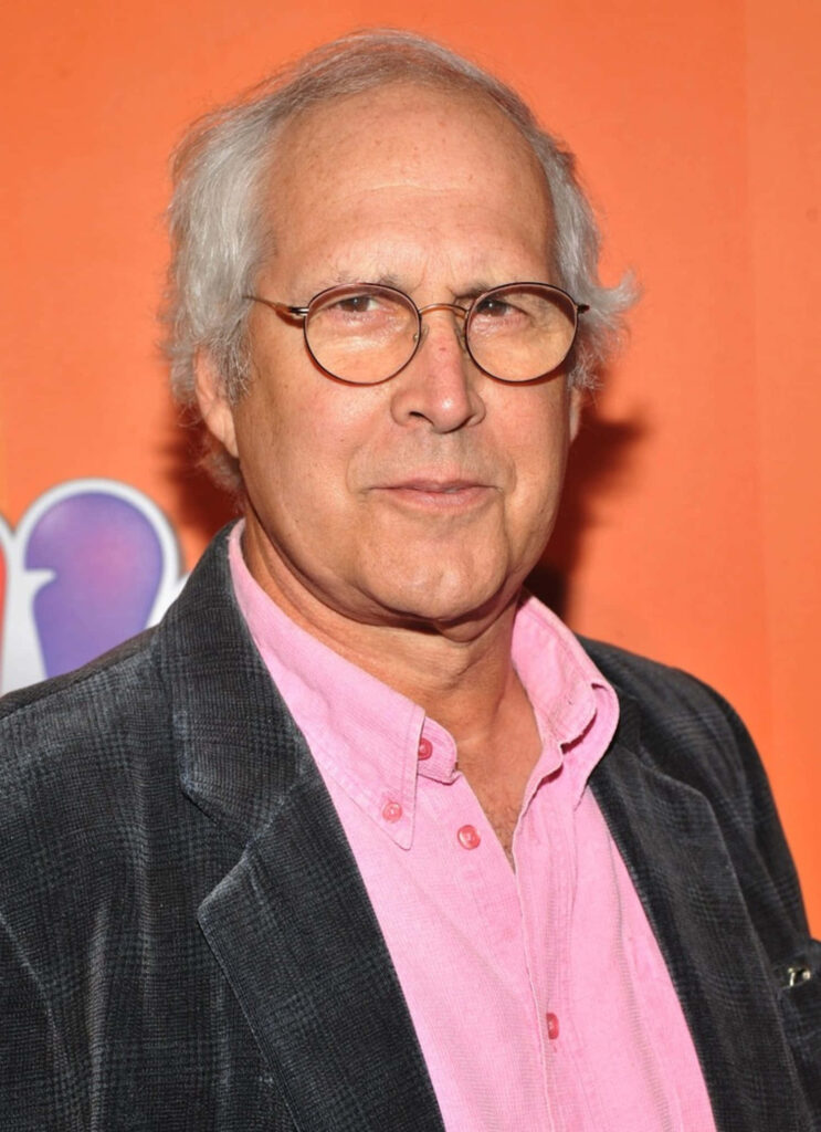 Chevy Chase candid portrait vibrant orange background pink shirt dark blazer round glasses wallpaper
