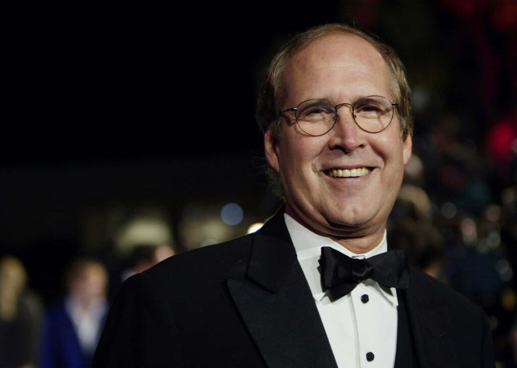 Chevy Chase in classic black tuxedo smiling warmly on dark blurred background wallpaper
