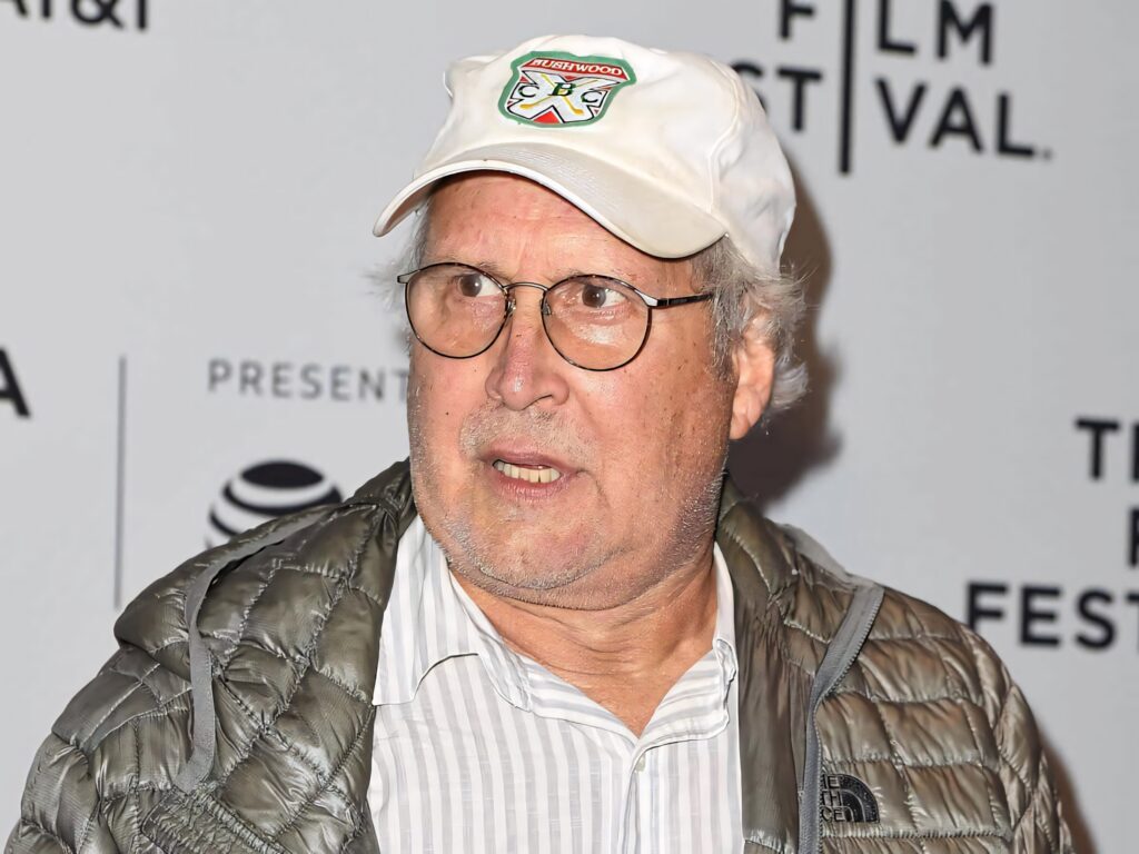 Chevy Chase candid portrait wearing quilted jacket striped shirt and Kenwood cap wallpaper background