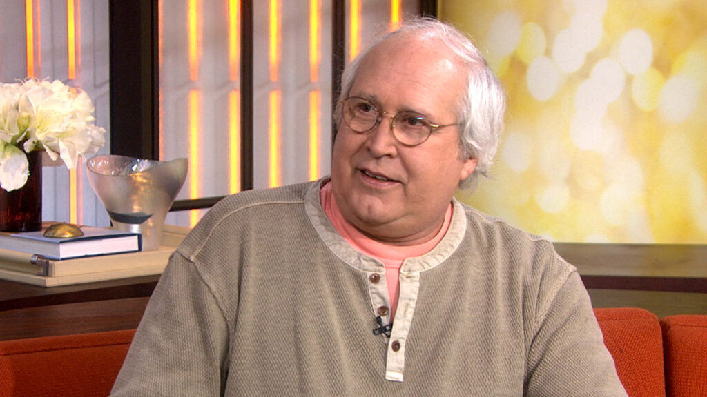 Chevy Chase in cozy interview setting with warm lighting and casual neutral outfit wallpaper