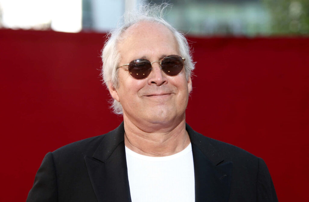 Chevy Chase confident pose wearing round sunglasses black jacket white shirt red background wallpaper