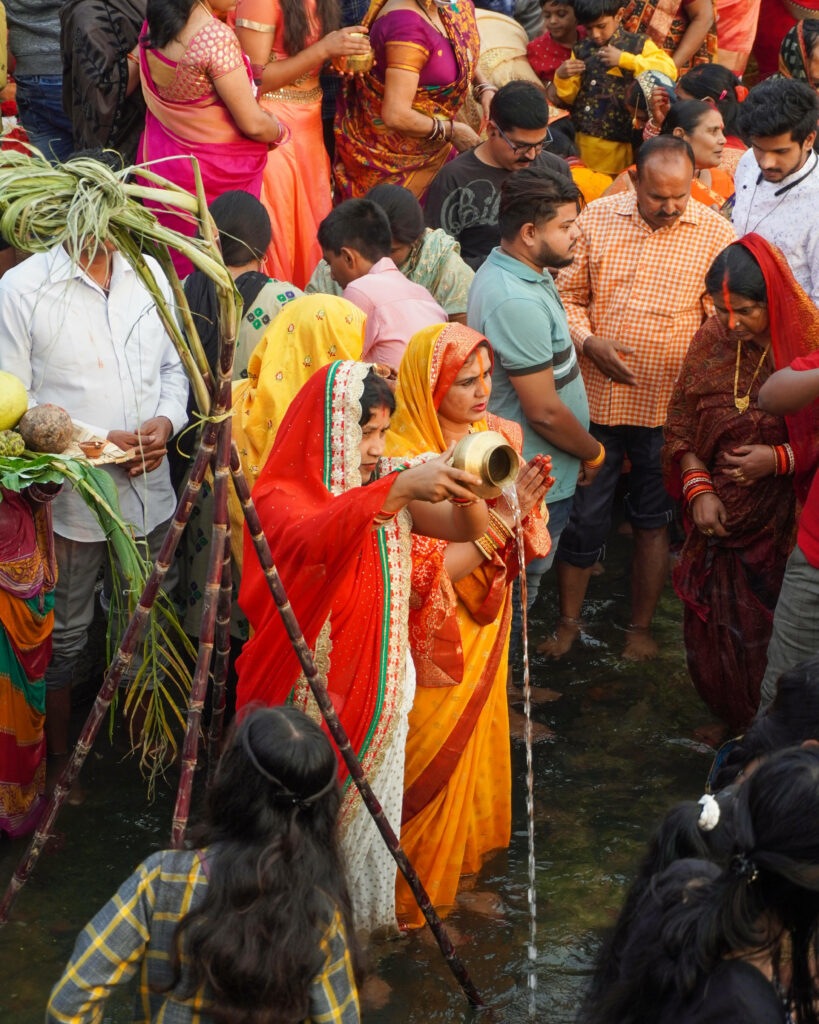 Devotees in colorful traditional clothes performing Chhath Puja rituals with feet submerged in water Wallpaper
